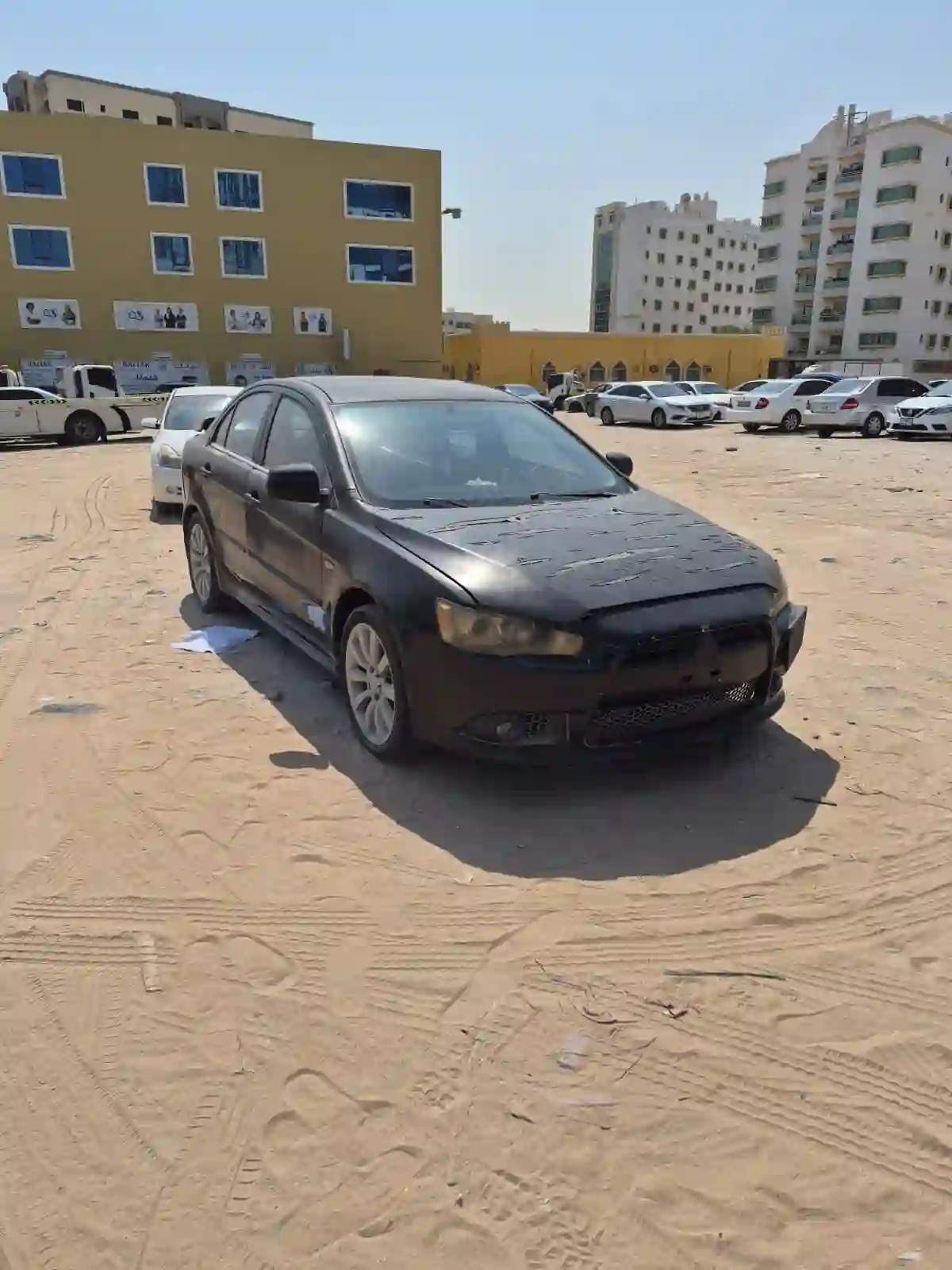 Black scrap Mitsubishi Lancer sedan in an open parking lot